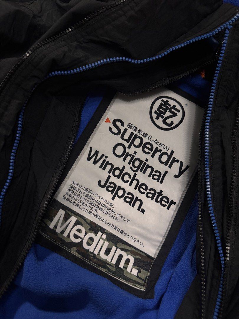 Superdry Original Windcheater Japan Black Jacket Medium (Category: Coats, Jackets and Outerwear) located in Alaminos. Submitted by outfitcheck.ph (Listing ID 1465109926, Image 2). Description: - Brand: Superdry Original Windcheater Japan - Color: Classic black with bright blue fleece lining - Size: Medium (based on inner label) - Features: Full zip closure, high neck collar, velcro storm flap - Details: Embroidered blue branding on shoulders, ora