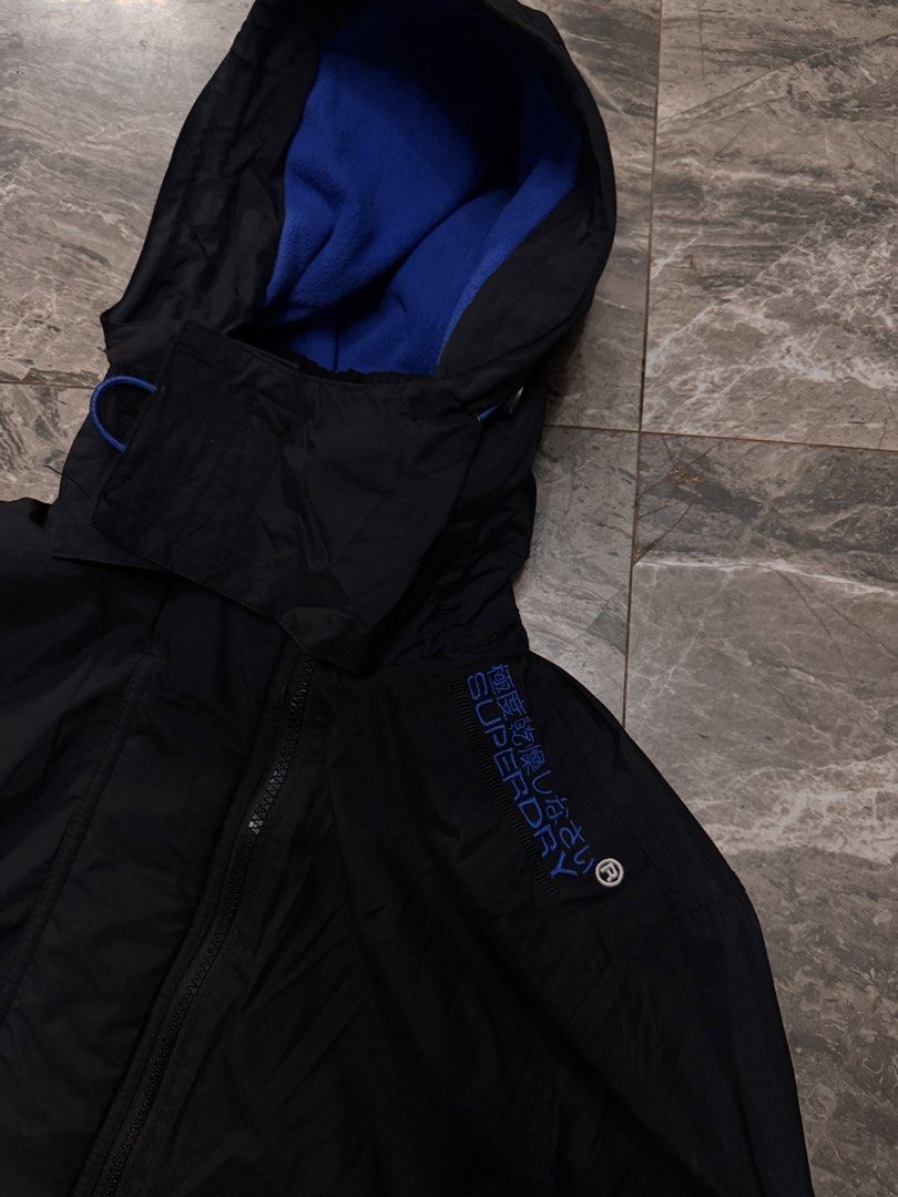 Superdry Original Windcheater Japan Black Jacket Medium (Category: Coats, Jackets and Outerwear) located in Alaminos. Submitted by outfitcheck.ph (Listing ID 1465109926, Image 3). Description: - Brand: Superdry Original Windcheater Japan - Color: Classic black with bright blue fleece lining - Size: Medium (based on inner label) - Features: Full zip closure, high neck collar, velcro storm flap - Details: Embroidered blue branding on shoulders, ora