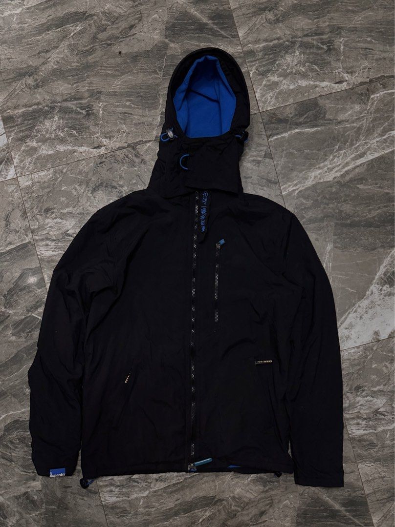 Superdry The Windhiker Jacket Black Blue Size M (Category: Coats, Jackets and Outerwear) located in Alaminos. Submitted by outfitcheck.ph (Listing ID 1465109768, Image 1). Description: - Brand: Superdry The Windhiker - Color: Black with bright blue inner fleece lining - Size: Medium (M) - Features: Full zip front, zippered chest pocket, and adjustable hood toggles - Details: Japanese character embroidery on storm flap and back right shoulder, plu