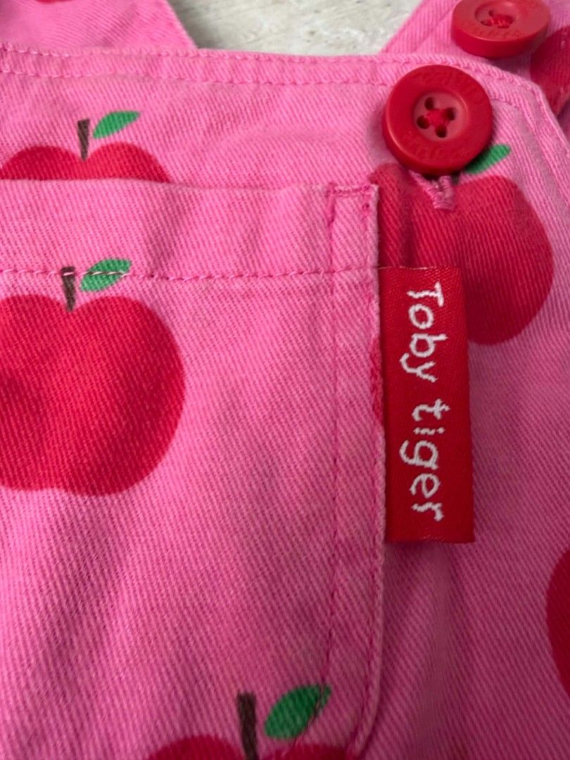 Toby Tiger Apple Print Pink Overalls (Category: Babies & Kids Fashion) located in Las Pinas. Submitted by pinkpototo36548 (Listing ID 1465071733, Image 3). Description: - Brand: Toby Tiger - Design: Pink overalls with all-over red apple print - Details: Red branded buttons on straps and sides - Pockets: Front chest pocket with red label tag and two back pockets - Style: Bright, playful, and comfortable for kids.