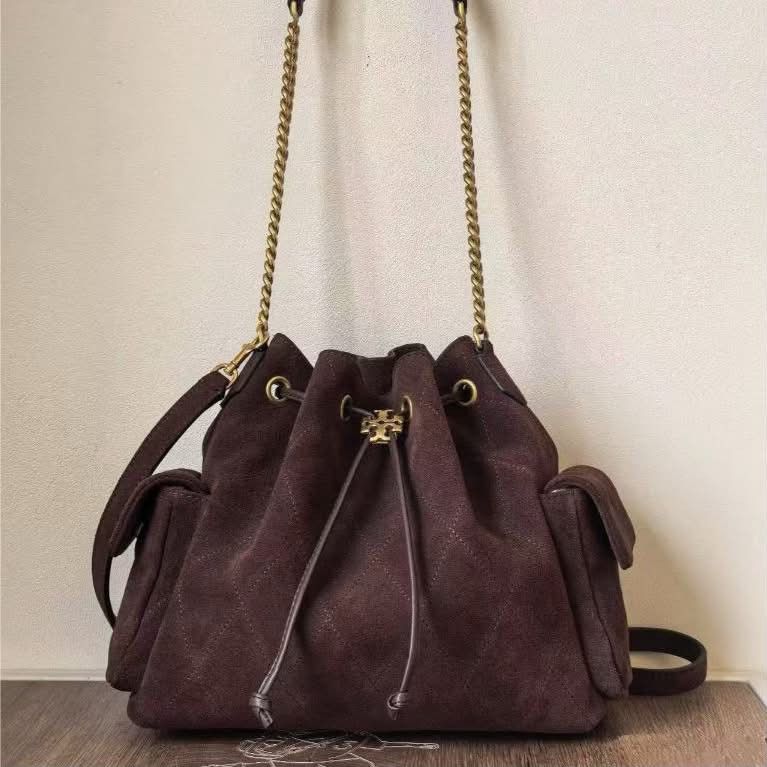 Tory Burch Brown Suede Bucket Bag (Category: Luxury Bags & Wallets) located in Paoay. Submitted by rvf1230 (Listing ID 1464977066, Image 3). Description: - Brand: Tory Burch bucket bag - Material: Rich brown suede with quilted diamond pattern - Hardware: Gold-tone accents and logo - Strap: Mixed chain and leather shoulder strap - Closure: Drawstring closure - Pockets: Two exterior side pockets with flaps and one interior zippered pocket - Conditi