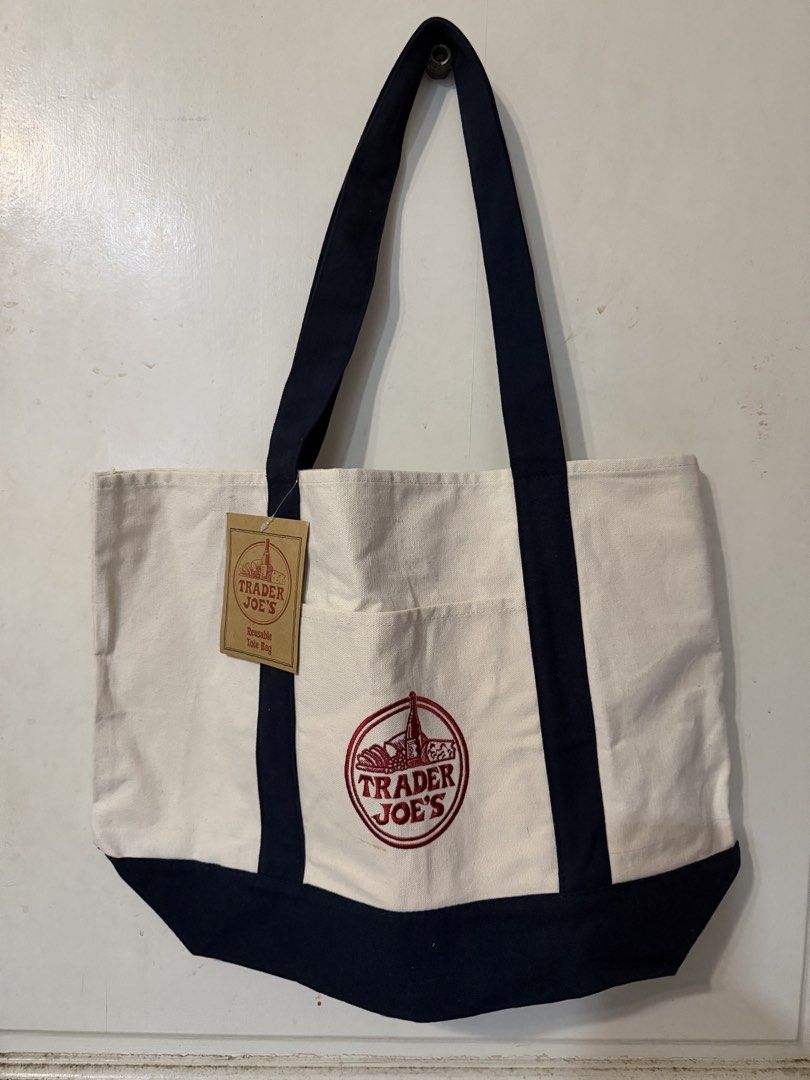 Trader Joe's Reusable Canvas Tote Bag (Category: Tote Bags) located in Quezon City. Submitted by kcobs (Listing ID 1465084115, Image 1). Description: - Authentic Trader Joe's canvas tote bag with original paper hang tag attached - Colorway: Off-white body with stylish navy blue handles and bottom block - Features a handy outer pocket with the embroidered Trader Joe's grocery round logo in red - Material: Durable blend of 65% cotton and 35% polyes