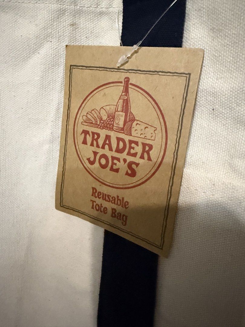 Trader Joe's Reusable Canvas Tote Bag (Category: Tote Bags) located in Quezon City. Submitted by kcobs (Listing ID 1465084115, Image 2). Description: - Authentic Trader Joe's canvas tote bag with original paper hang tag attached - Colorway: Off-white body with stylish navy blue handles and bottom block - Features a handy outer pocket with the embroidered Trader Joe's grocery round logo in red - Material: Durable blend of 65% cotton and 35% polyes