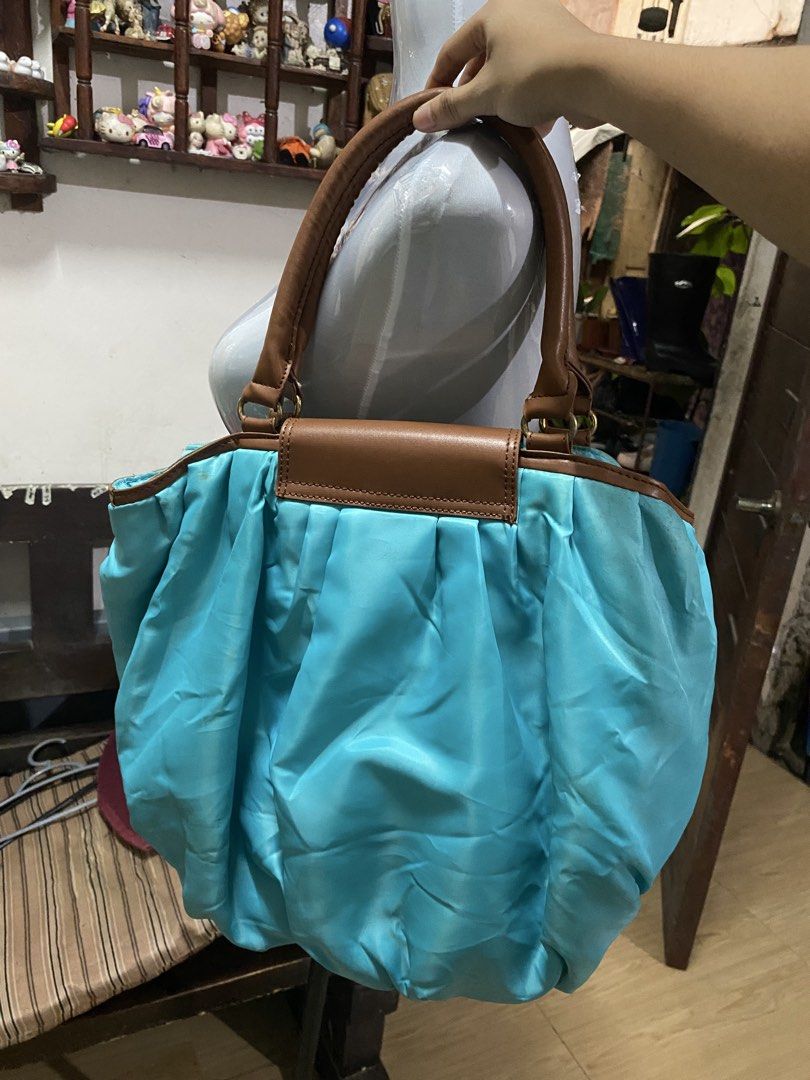 Turquoise Shoulder Bag with Brown Handles (Category: Tote Bags) located in Lingayen. Submitted by suika_thrift05 (Listing ID 1465085491, Image 2). Description: - Color: Bright blue with brown faux leather trim - Material: Durable nylon body with faux leather top handles - Closure: Front magnetic flap - Interior: Roomy and slouchy, with some staining and discoloration marks near the pocket and lining - Condition: Pre-loved, ready for a new home!.