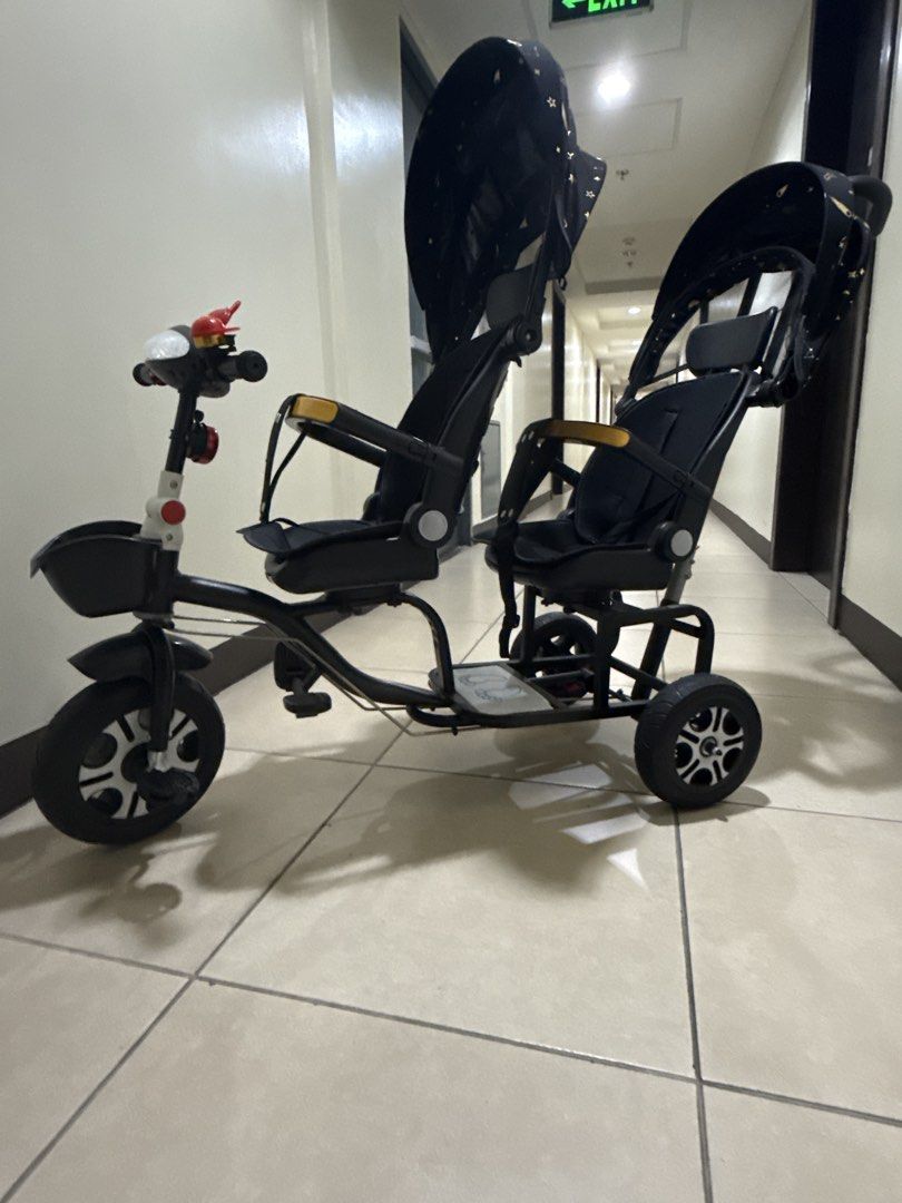 Twin Tandem Stroller Tricycle Black Gold Star Pattern (Category: Strollers) located in Taguig. Submitted by hiddenclosetasia (Listing ID 1465077083, Image 1). Description: - Double seating tandem tricycle perfect for twins or siblings - Stylish black frame with matching black and gold star canopy - Parent push handle at the back and front pedals for riding - Equipped with two safety bars, footrests, and a small front basket , bike bell - Clean, w