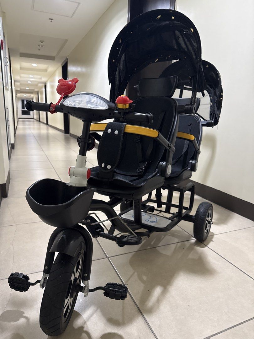 Twin Tandem Stroller Tricycle Black Gold Star Pattern (Category: Strollers) located in Taguig. Submitted by hiddenclosetasia (Listing ID 1465077083, Image 3). Description: - Double seating tandem tricycle perfect for twins or siblings - Stylish black frame with matching black and gold star canopy - Parent push handle at the back and front pedals for riding - Equipped with two safety bars, footrests, and a small front basket , bike bell - Clean, w