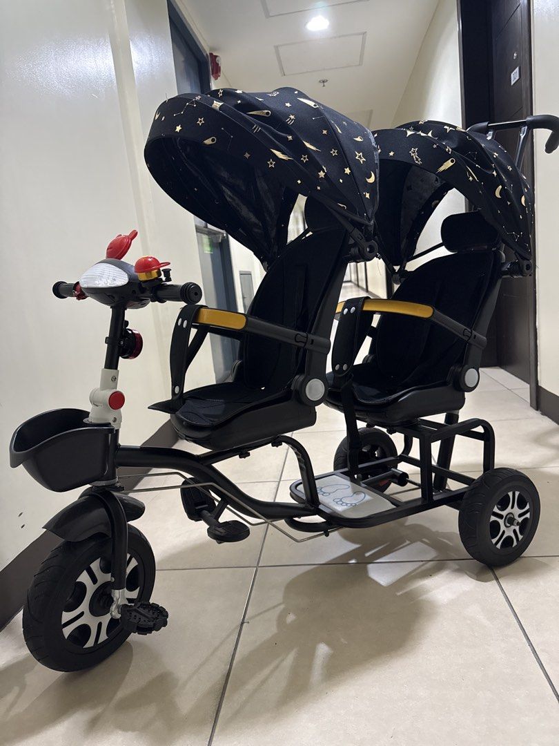 Twin Tandem Stroller Tricycle Black Gold Star Pattern (Category: Strollers) located in Taguig. Submitted by hiddenclosetasia (Listing ID 1465077083, Image 2). Description: - Double seating tandem tricycle perfect for twins or siblings - Stylish black frame with matching black and gold star canopy - Parent push handle at the back and front pedals for riding - Equipped with two safety bars, footrests, and a small front basket , bike bell - Clean, w