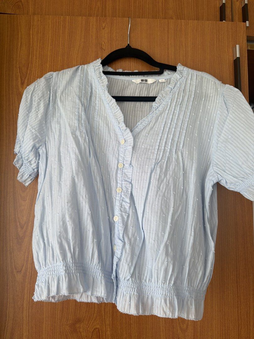 Uniqlo Light Blue Short Sleeve Blouse (Category: Blouses) located in Cavite. Submitted by klarev (Listing ID 1464997069, Image 1). Description: - Brand: Uniqlo - Size: Medium (M) - Color: Light blue - Material/Design: Textured dotted fabric with subtle vertical stripes - Details: Ruffled trim along V-neckline and button placket, pearl-style white buttons.