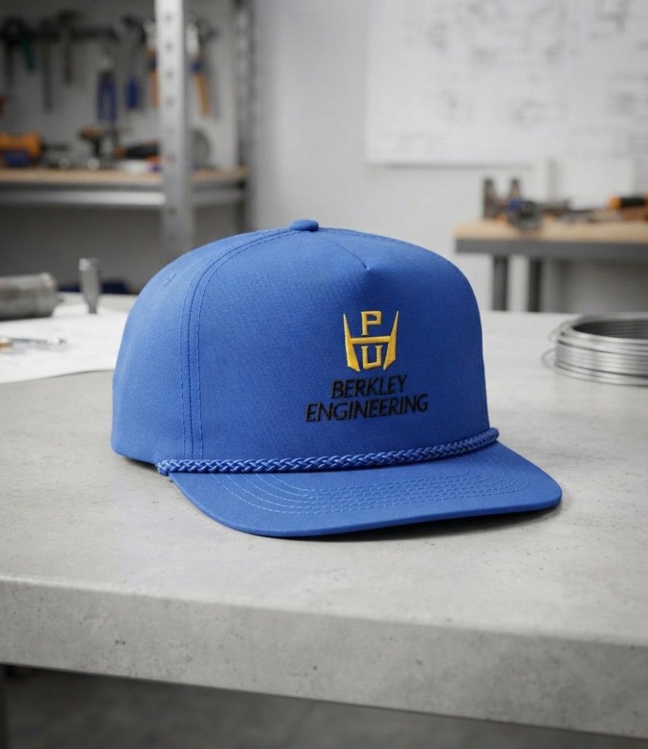 Vintage Berkley Engineering Snapback Hat, Blue with Yellow Logo (Category: Caps & Hats) located in Binangonan. Submitted by yuristalin888 (Listing ID 1464973369, Image 1). Description: This vintage blue snapback hat features the "Berkley Engineering" logo embroidered in yellow on the front. The hat has a classic five-panel construction with a rope detail across the brim. It is made of a sturdy fabric and includes an adjustable strap and brass-ton