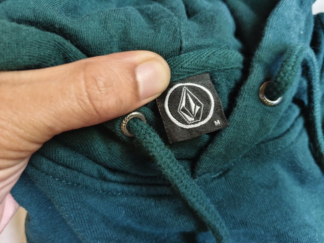 Volcom Green Hoodie Sweatshirt Size M (Category: Coats, Jackets and Outerwear) located in Baguio. Submitted by thriftjc (Listing ID 1464973364, Image 2). Description: - Brand: Volcom - Color: Dark green - Size: M (tagged on collar) - Material: 60% cotton, 40% polyester - Design: Big stone logo printed on the chest - Features: Kangaroo front pocket, adjustable drawstring hood, ribbed cuffs and hem - Origin: Made in China.