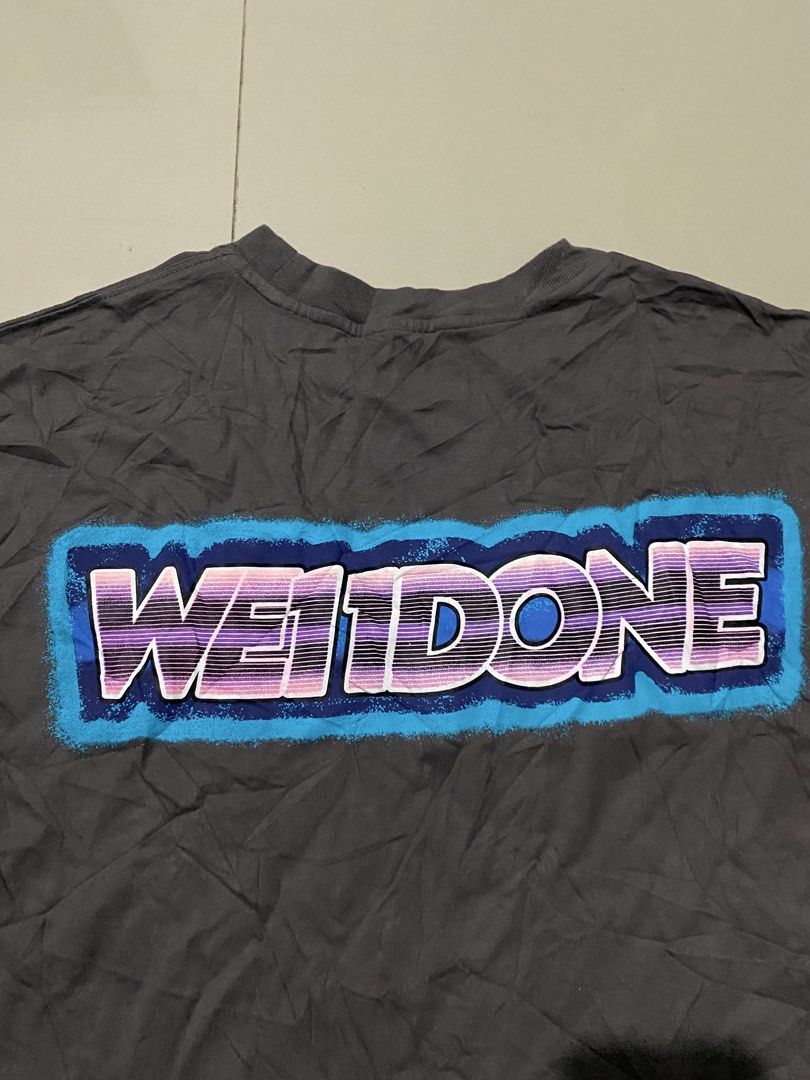 WE11DONE Grey Short Sleeve T-Shirt (Category: Tshirts & Polo Shirts ) located in Makati City. Submitted by dymon_08 (Listing ID 1465101942, Image 2). Description: - Brand: WE11DONE - Dimes W16.5 L18 - Color: Dark grey - Fit: Relaxed streetwear fit with crew neck - Details: Small box logo on chest, bold colorful lettering graphic on the back - Condition: Excellent, clean fabric with no stains or rips - Perfect everyday tee to style with jeans or c