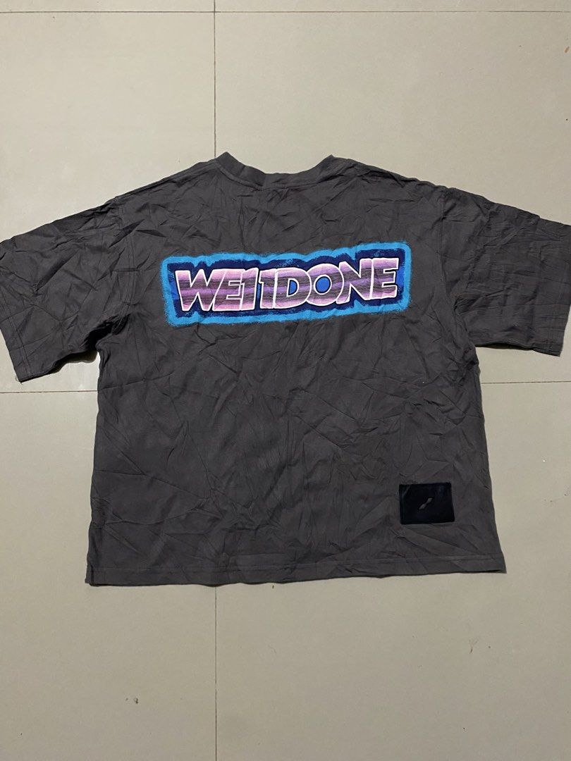 WE11DONE Grey Short Sleeve T-Shirt (Category: Tshirts & Polo Shirts ) located in Makati City. Submitted by dymon_08 (Listing ID 1465101942, Image 1). Description: - Brand: WE11DONE - Dimes W16.5 L18 - Color: Dark grey - Fit: Relaxed streetwear fit with crew neck - Details: Small box logo on chest, bold colorful lettering graphic on the back - Condition: Excellent, clean fabric with no stains or rips - Perfect everyday tee to style with jeans or c