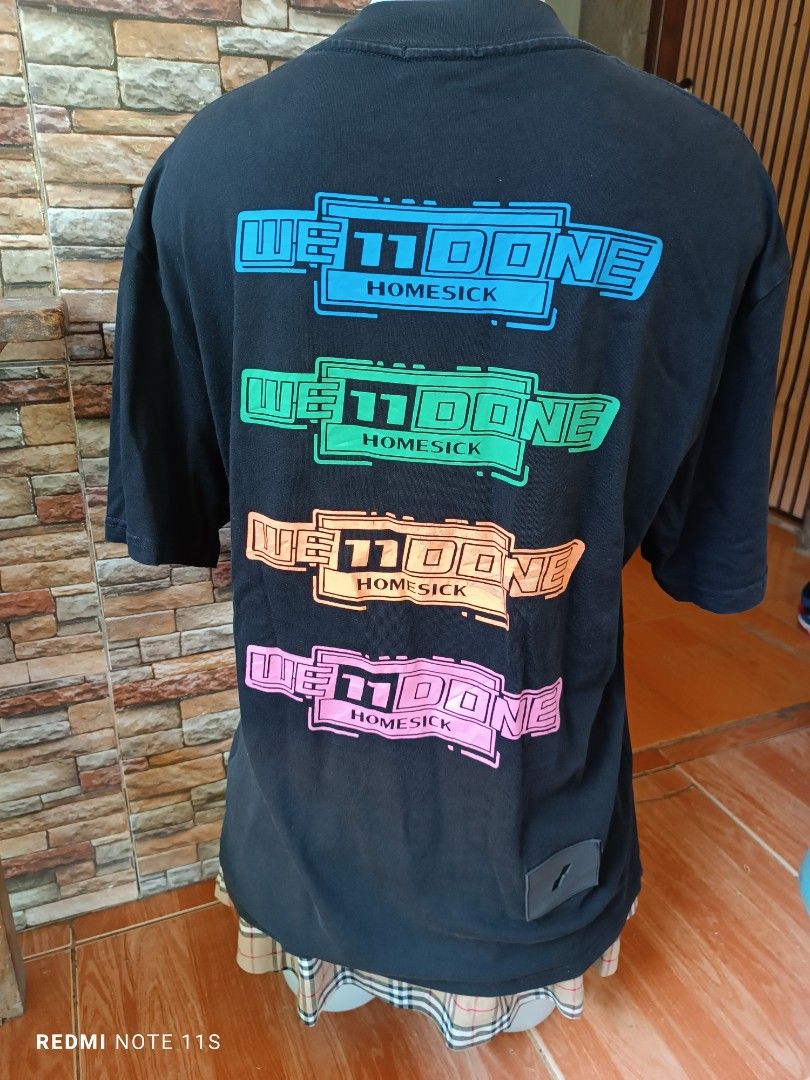 WE11DONE Homesick Black T-Shirt (Category: Tshirts & Polo Shirts ) located in Gapan. Submitted by thrift2heaven (Listing ID 1465088344, Image 2). Description: Black WE11DONE t-shirt with multicolored Homesick text graphics stacked on the back. Small pink logo patch on the chest. Ribbed crew neckline and rubber brand label near the hem. Inner collar tag and authenticity QR code label attached. Relaxed fit style..