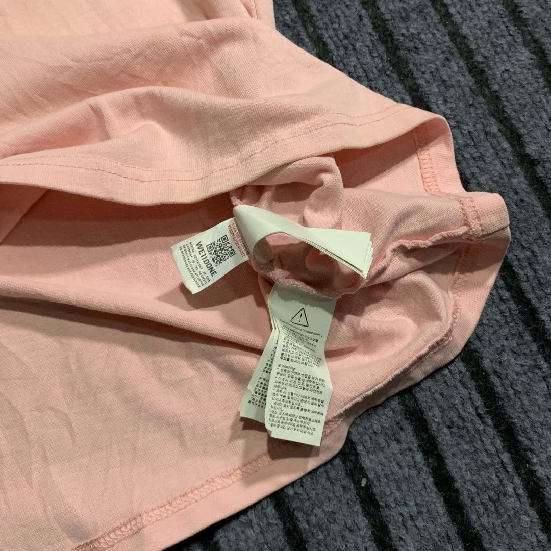 We11done Pink Logo T-Shirt (Category: Tshirts & Polo Shirts ) located in Bulacan. Submitted by lzl_thriftfinds (Listing ID 1465098273, Image 2). Description: - Brand: We11done - Color: Pink - Size: 23Wx29L - Fit: Relaxed fit with classic crew neck - Design: Black logo lettering and central square patch graphic on the chest - Details: Includes interior authenticity tags and a care label stitched near the hem.