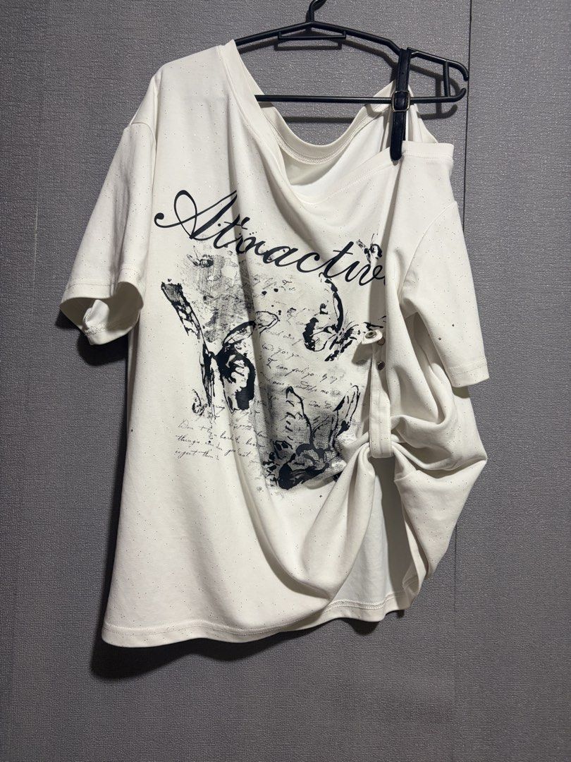 White Graphic Off-Shoulder T-Shirt with Strap (Category: Shirts) located in Manila. Submitted by wildriver.e8b64e (Listing ID 1465081068, Image 1). Description: Fit up to XL - Color: White with speckled pattern and black butterfly graphic - Text: 'Attractive' script detail - Design: Oversized loose fit with rolled side gathering - Neckline: Asymmetrical with a built-in black shoulder strap - Style: Trendy casual streetwear.