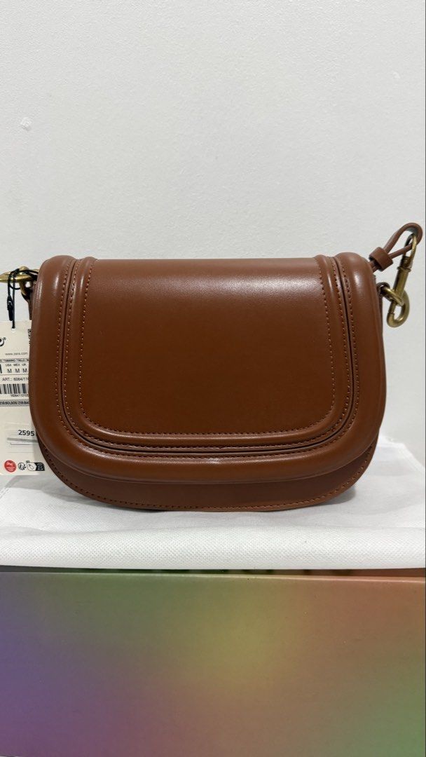 Zara Brown Crossbody Saddle Bag (Category: Cross-body Bags) located in Quezon City. Submitted by thriftjunkiephl (Listing ID 1465014055, Image 3). Description: - Brand new with original store tags attached - Rich brown color with chic tonal stitching and structured saddle shape - Secure foldover flap design with magnetic snap closure - Elegant gold-tone hardware - Includes a detachable strap (neatly folded inside) for versatile styling - Stored w