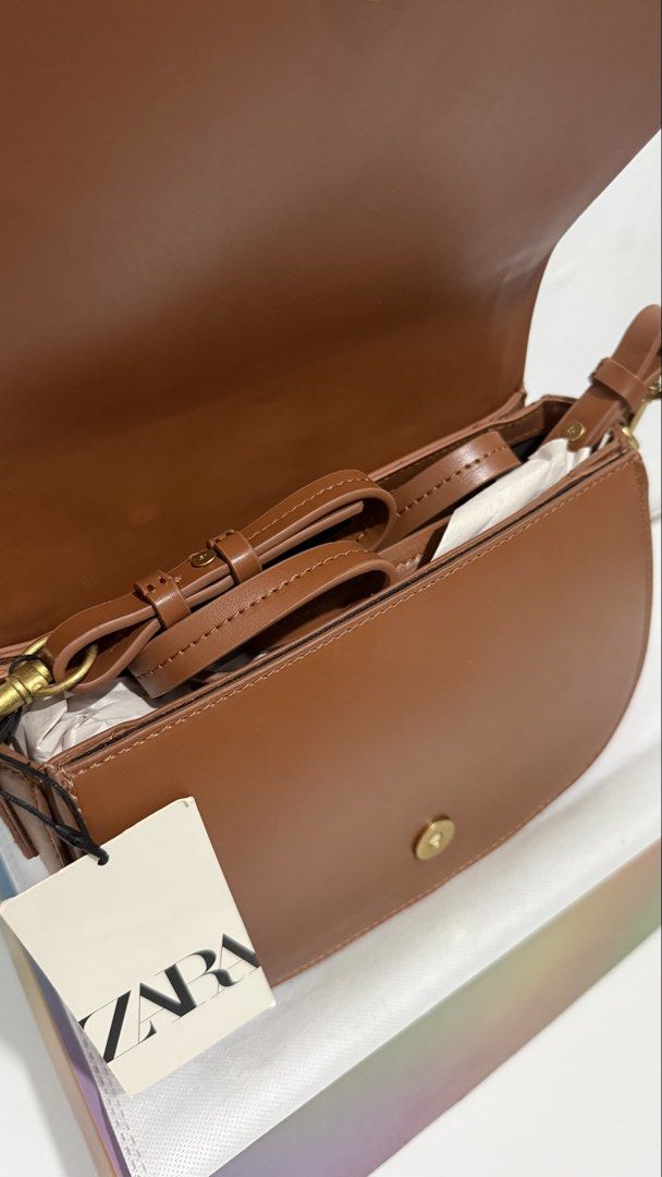 Zara Brown Crossbody Saddle Bag (Category: Cross-body Bags) located in Quezon City. Submitted by thriftjunkiephl (Listing ID 1465014055, Image 2). Description: - Brand new with original store tags attached - Rich brown color with chic tonal stitching and structured saddle shape - Secure foldover flap design with magnetic snap closure - Elegant gold-tone hardware - Includes a detachable strap (neatly folded inside) for versatile styling - Stored w