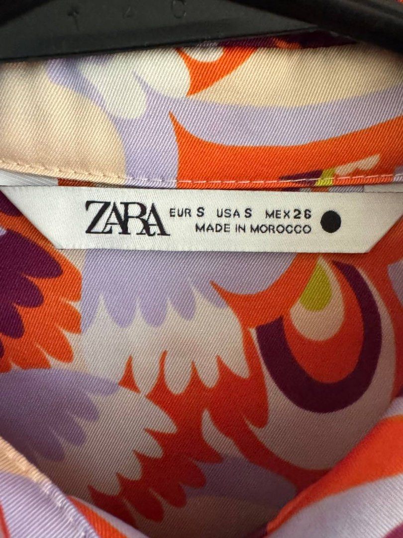 Zara Retro Floral Print Button-Down Shirt Size S (Category: Blouses) located in Taguig. Submitted by anxmz (Listing ID 1465043381, Image 2). Description: - Brand: Zara - Design: 70s-style abstract floral print - Colors: Orange, purple, lilac, and cream - Details: Collared neckline, front button closure, one chest pocket - Fabric: Silky, lightweight, and flowy - Origin: Made in Morocco - Condition/Use: Great statement piece for everyday wear.