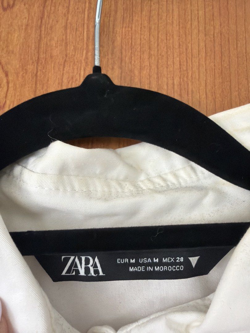Zara White Cropped Button-Up Shirt (Category: Shirts) located in Cavite. Submitted by klarev (Listing ID 1465011127, Image 3). Description: - Brand: Zara - Style: Cropped button-up shirt with long sleeves, cuffs, classic collar, and buttoned sleeves - Color: White - Flaws: Small hole near the pocket and slight discoloration around the inner collar area.