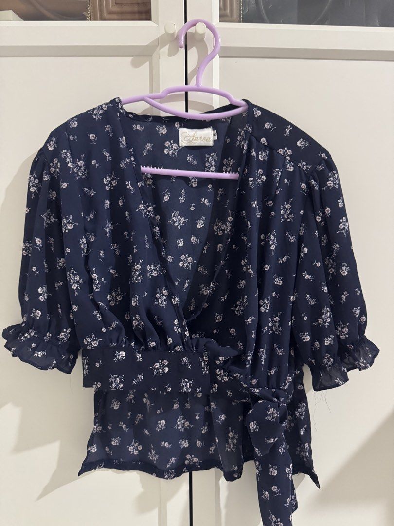 Aurea Navy Floral Wrap Top Size M (Category: Blouses) located in Mangatarem. Submitted by jvleexx (Listing ID 1459626321, Image 1). Description: - Navy blue top with a charming white floral print. - Flattering wrap style with a convenient side tie closure. - Features short sleeves with a delicate ruffle detail at the hem. - Made from a lightweight fabric, ideal for comfortable, casual outings. - Versatile piece that can be dressed up or down..