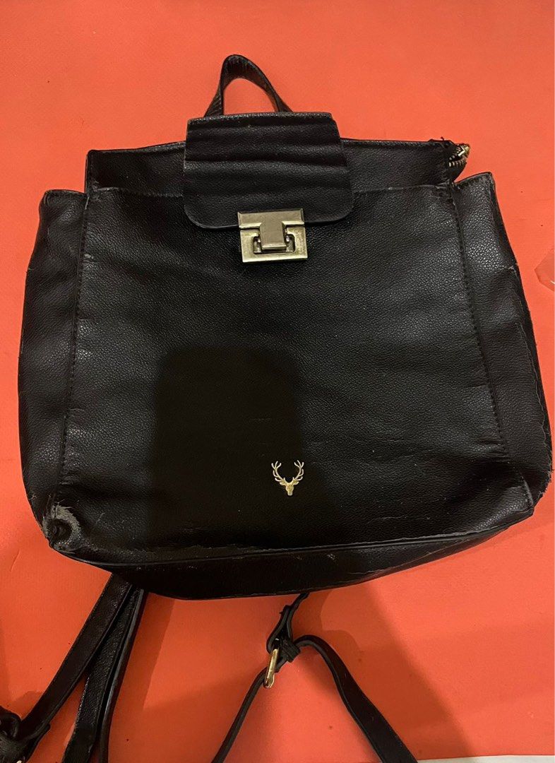 Black Faux Leather Backpack with Deer Logo (Category: Backpacks) located in Manila. Submitted by jana0011 (Listing ID 1459683573, Image 1). Description: - Black backpack - Gold deer logo on front - Flap closure with metal clasp - Adjustable straps - Minor wear on bottom corners - Ideal for everyday use.