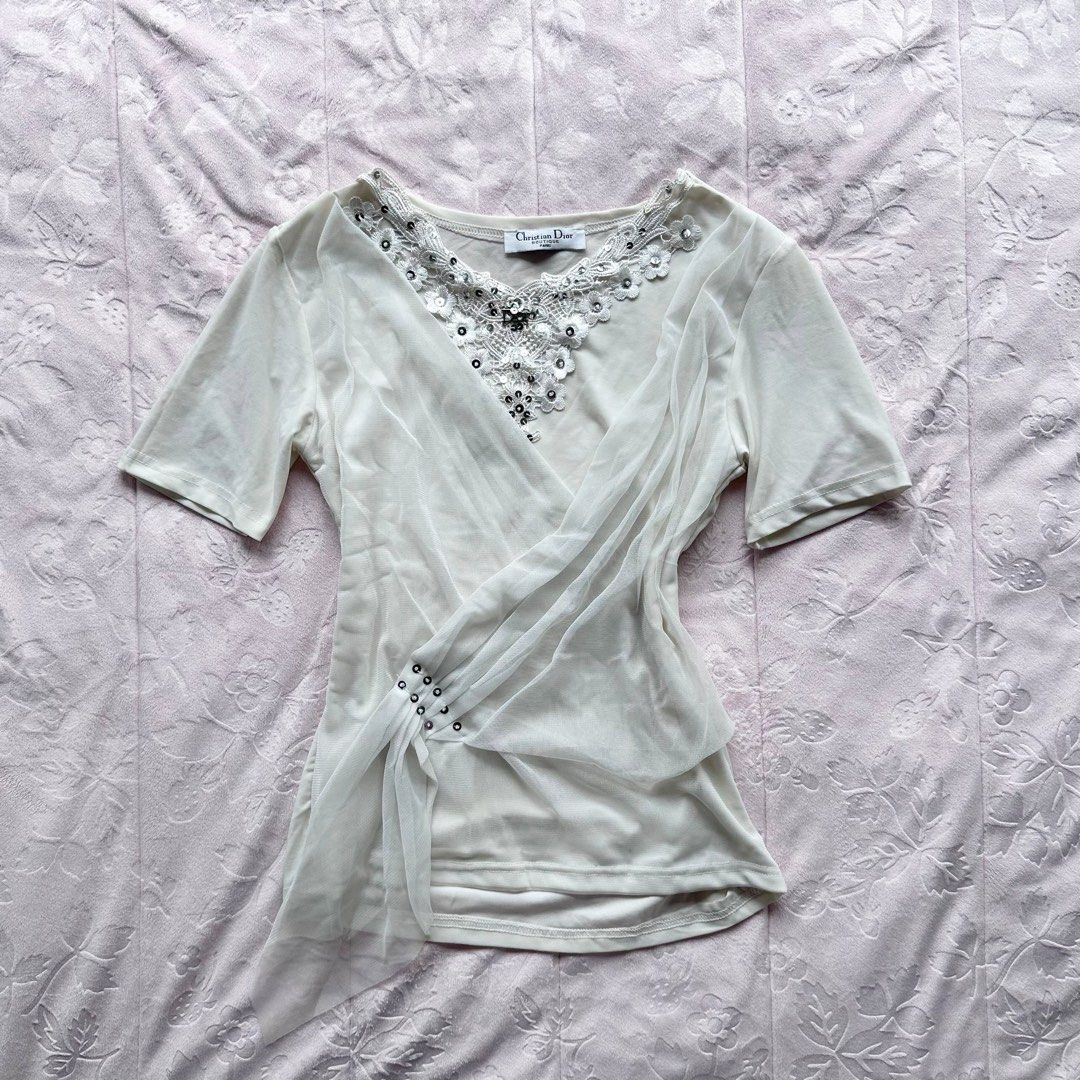 CHRISTIAN DIOR Couture Wrap Top (Category: Blouses) located in San Fernando. Submitted by rianne_von (Listing ID 1459619055, Image 1). Description: W: 15 in L: 20.5 in info: ✧ ivory wrap-style top w/ sheer mesh overlay + draped side detailing ✧ ornate floral lace neckline w/ sequins, beads + Dior logo embellishment ✧ very good thrifted condition; minimal faded stain observed, otherwise no major flaws ✧ color may vary slightly due to lighting.