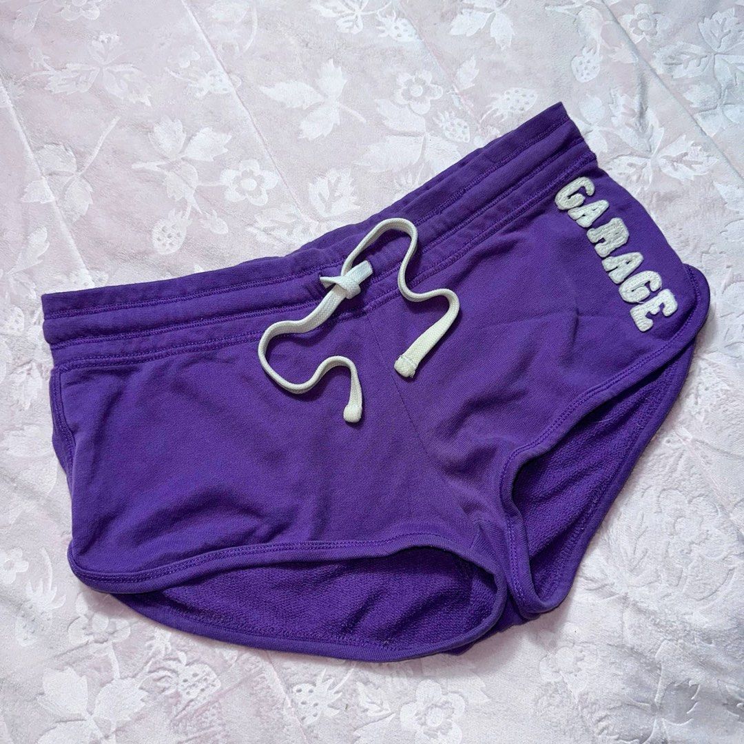 GARAGE Purple Dolphin Shorts (Category: Shorts) located in San Fernando. Submitted by rianne_von (Listing ID 1459590631, Image 2). Description: Size XS on tag W: 16 in L: 8 in info: ✧ vibrant purple short shorts w/ contrast white drawstring ✧ embroidered GARAGE lettering + curved dolphin hem for a sporty Y2K look ✧ very good thrifted condition; minimal faded stain observed, otherwise no major flaws ✧ color may vary slightly due to lighting .