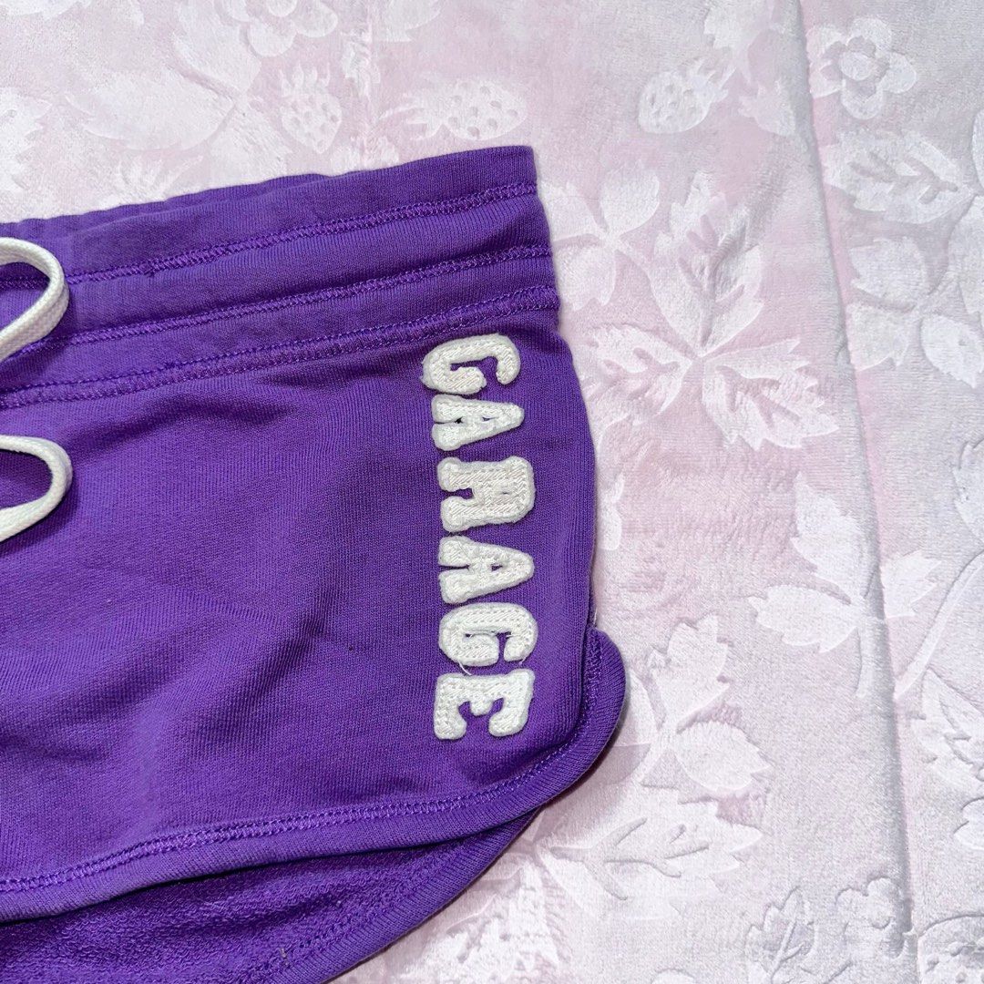 GARAGE Purple Dolphin Shorts (Category: Shorts) located in San Fernando. Submitted by rianne_von (Listing ID 1459590631, Image 3). Description: Size XS on tag W: 16 in L: 8 in info: ✧ vibrant purple short shorts w/ contrast white drawstring ✧ embroidered GARAGE lettering + curved dolphin hem for a sporty Y2K look ✧ very good thrifted condition; minimal faded stain observed, otherwise no major flaws ✧ color may vary slightly due to lighting .