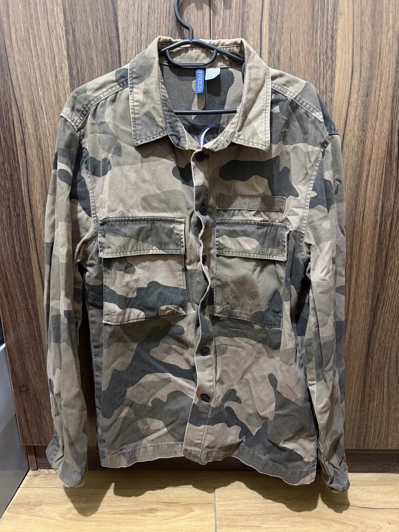 H&M Camo Jacket with Purple Embroidery (Category: Coats, Jackets and Outerwear) located in Taguig. Submitted by plfits (Listing ID 1459663125, Image 1). Description: - H&M Camouflage Jacket - Size: Medium (M) - Bold purple embroidered text on the back - Two chest pockets - Button-up front - Ideal for layering.