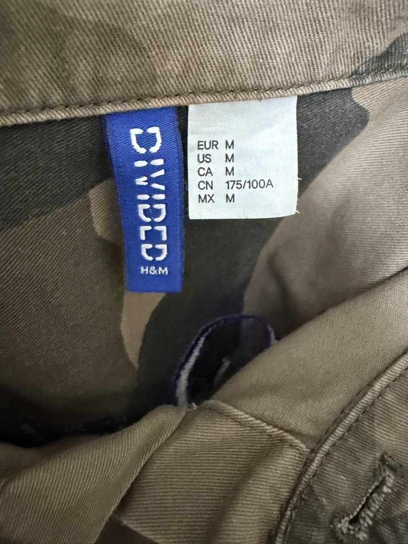 H&M Camo Jacket with Purple Embroidery (Category: Coats, Jackets and Outerwear) located in Taguig. Submitted by plfits (Listing ID 1459663125, Image 3). Description: - H&M Camouflage Jacket - Size: Medium (M) - Bold purple embroidered text on the back - Two chest pockets - Button-up front - Ideal for layering.