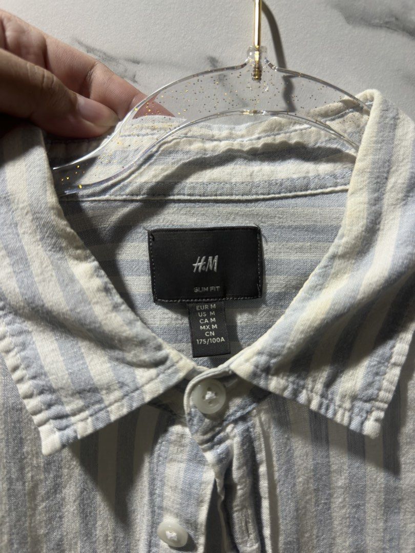 H&M Slim Fit Striped Button-Up Shirt (Category: Tshirts & Polo Shirts ) located in Baguio. Submitted by miss_misery (Listing ID 1459641504, Image 2). Description: - H&M Slim Fit Shirt - Color: Light blue and white vertical stripes - Style: Button-up front with collar - Sleeves: Long sleeves - Occasion: Perfect for casual wear or dressing up - Sizing: Please refer to the tag for specific size details.