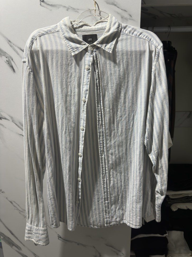 H&M Slim Fit Striped Button-Up Shirt (Category: Tshirts & Polo Shirts ) located in Baguio. Submitted by miss_misery (Listing ID 1459641504, Image 1). Description: - H&M Slim Fit Shirt - Color: Light blue and white vertical stripes - Style: Button-up front with collar - Sleeves: Long sleeves - Occasion: Perfect for casual wear or dressing up - Sizing: Please refer to the tag for specific size details.