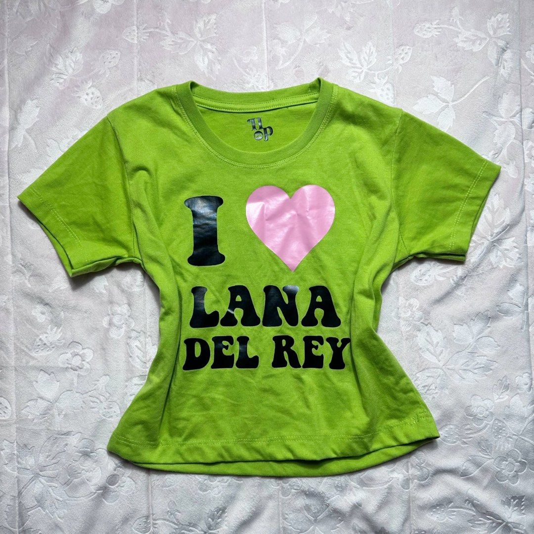 Lime Green Statement Shirt (Category: Shirts) located in San Fernando. Submitted by rianne_von (Listing ID 1459614388, Image 1). Description: Size S on tag W: 16 in L: 17 in info: ✧ vibrant lime green fitted baby tee w/ bold “I ♥ LANA DEL REY” front graphic ✧ contrast black lettering + pink satin-style heart detail for a Y2K pop aesthetic ✧ excellent thrifted condition; no holes, stains, or major flaws observed ✧ color may vary slightly due to li