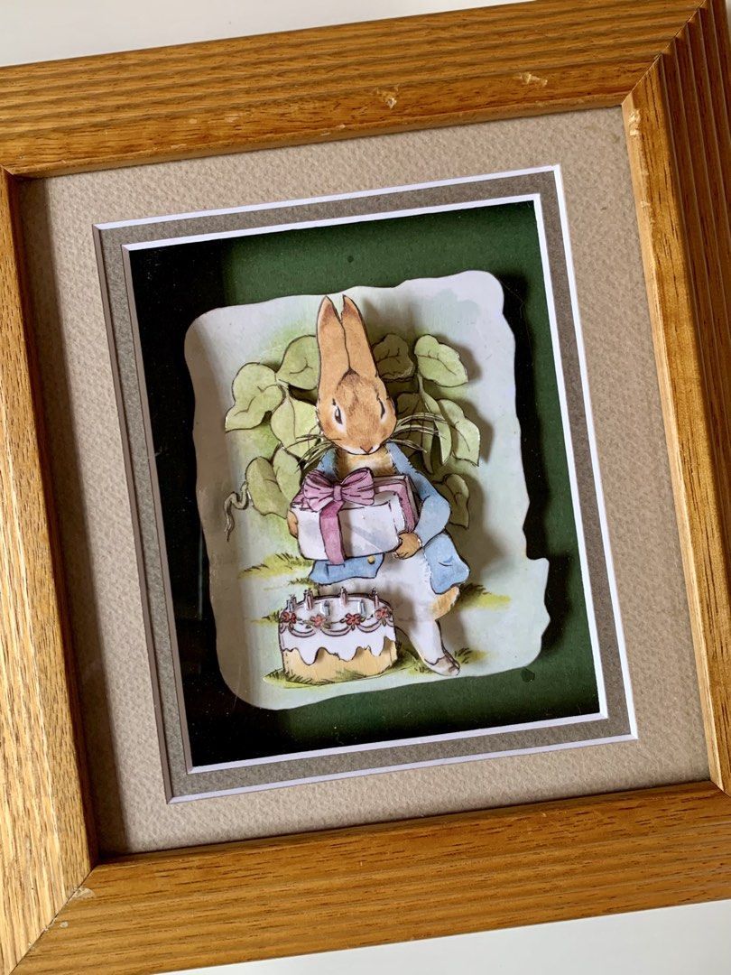 vintage Peter Rabbit 3D decoupage art piece - wallframe (Category: Wall Decor) located in Tandag. Submitted by jeason_22 (Listing ID 1459593049, Image 2). Description: Design Features Style: 3D decoupage or shadow box art, where paper layers are cut and stacked to create depth. Scene: Peter Rabbit wears his classic blue jacket, holds a wrapped gift with a pink bow, and stands near a small birthday cake with candles. Frame: Set inside a textured, 