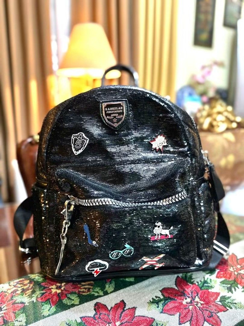 Black Sequin Backpack with Charms (Category: Backpacks) located in Santo Domingo. Submitted by krizzies_korner (Listing ID 1459740568, Image 1). Description: - Eye-catching sparkly black backpack covered in sequins. - Features a spacious main zippered compartment. - Includes a convenient front pocket for quick access. - Comes with adorable enamel pins and a fun keychain. - Versatile for everyday use or adding flair to a night out. - Packed with l