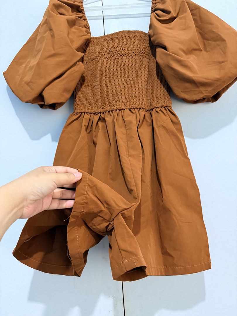 Brown Smocked Puff Sleeve Square Neck Romper (Category: Dresses) located in Las Pinas. Submitted by goldenoona_ (Listing ID 1459758617, Image 2). Description: - Brown romper - Smocked bodice - Puff sleeves - Square neckline - Flowy skirt - Tag indicates size medium - Ideal for casual outings or parties - Comfortable and stylish.