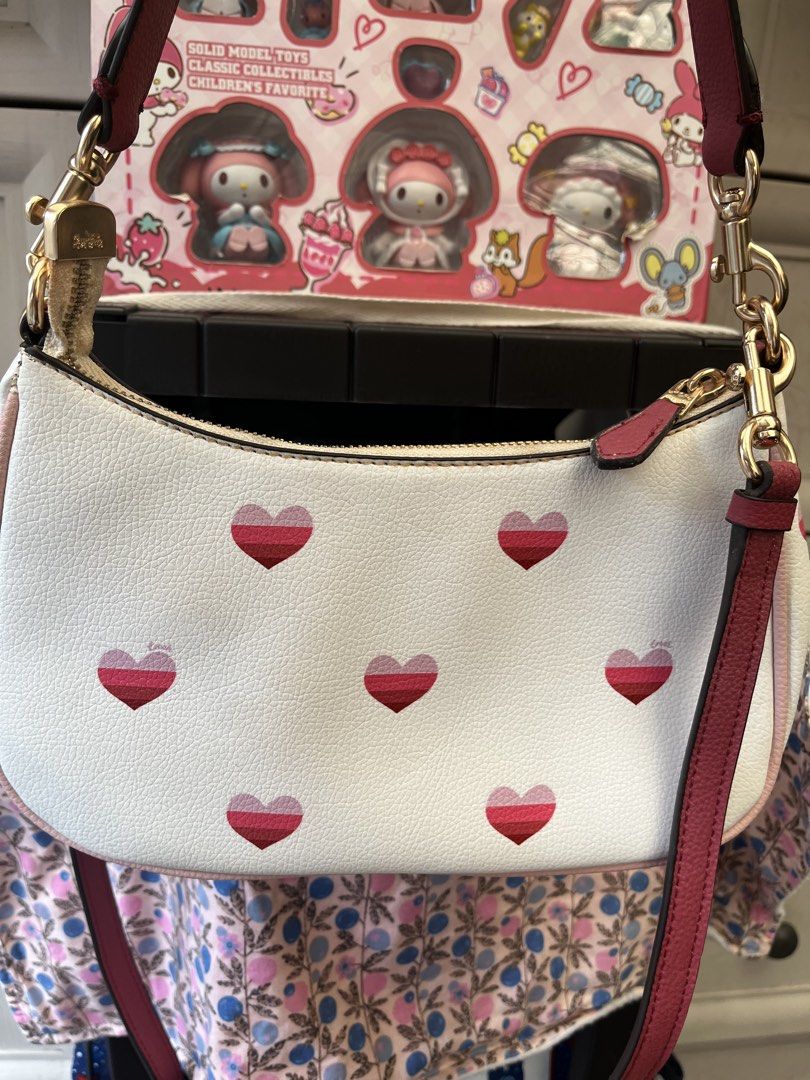 Coach White Heart Print Shoulder Bag (Category: Cross-body Bags) located in Pasig City. Submitted by melaiski28 (Listing ID 1459849555, Image 2). Description: - White Coach shoulder bag - Adorable pink and red heart print - Gold hardware and chain strap - Small stain on front near logo - Perfect size for essentials.