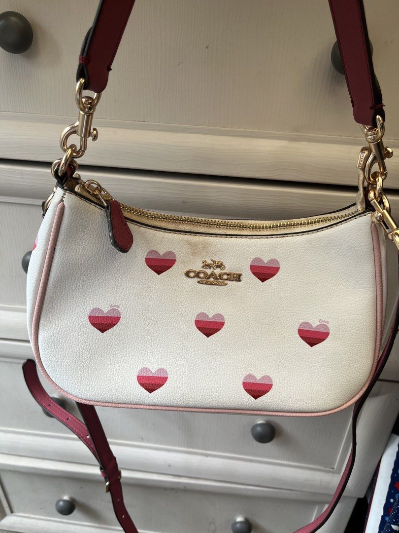 Coach White Heart Print Shoulder Bag (Category: Cross-body Bags) located in Pasig City. Submitted by melaiski28 (Listing ID 1459849555, Image 3). Description: - White Coach shoulder bag - Adorable pink and red heart print - Gold hardware and chain strap - Small stain on front near logo - Perfect size for essentials.