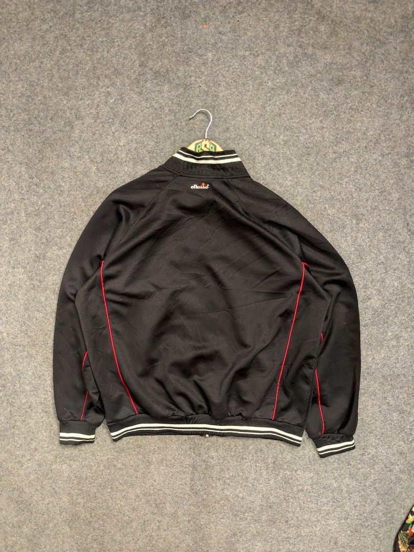 Ellesse Black Track Jacket with Red Piping (Category: Coats, Jackets and Outerwear) located in Cordova. Submitted by bsb.streetluxvintage.clothing (Listing ID 1459797764, Image 2). Description: - Classic black Ellesse track jacket - Red piping along the sides - White striped cuffs and collar - Full zip closure - Embroidered Ellesse logo on chest and back - Ideal for casual wear or sports.