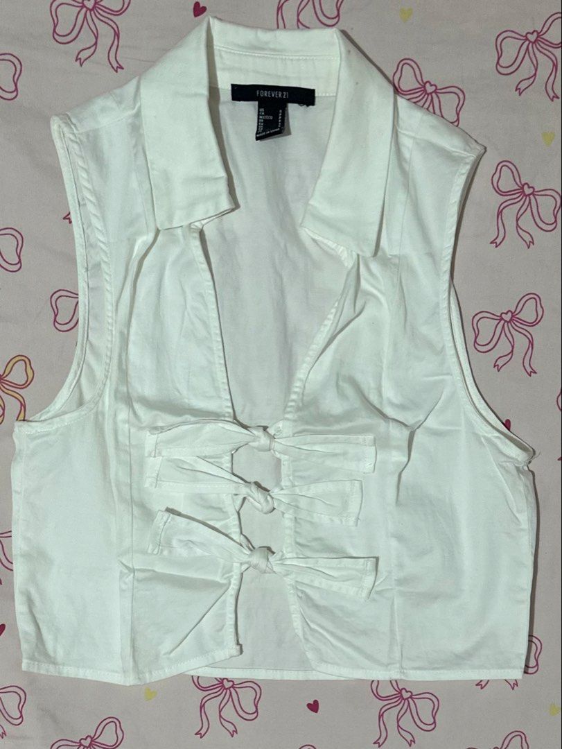 Forever 21 White Sleeveless Cropped Collared Top with Bows (Category: Sleeveless) located in Daet. Submitted by 614cb (Listing ID 1459719210, Image 1). Description: - White sleeveless crop top - Brand: Forever 21 - Features: Collared neckline, V-cut front with 3 bow details - Back: Plain - Measurements: Approx. 15 inches across the chest Used once Has stains can be seen in the photos due to storage Still very pretty Rfs: been wfh and seldom goes 