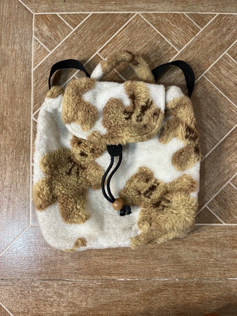 Fuzzy Bear Design Backpack (Category: Backpacks) located in Gapan. Submitted by lunashop14 (Listing ID 1459762446, Image 1). Description: - Adorable fuzzy backpack with a cow print design. - Made from soft white and brown fuzzy material. - Features a secure drawstring closure with a wooden bead accent. - Adjustable black straps for comfortable carrying. - Durable tan canvas material on the back. - Includes a small inner pocket with a snap closure