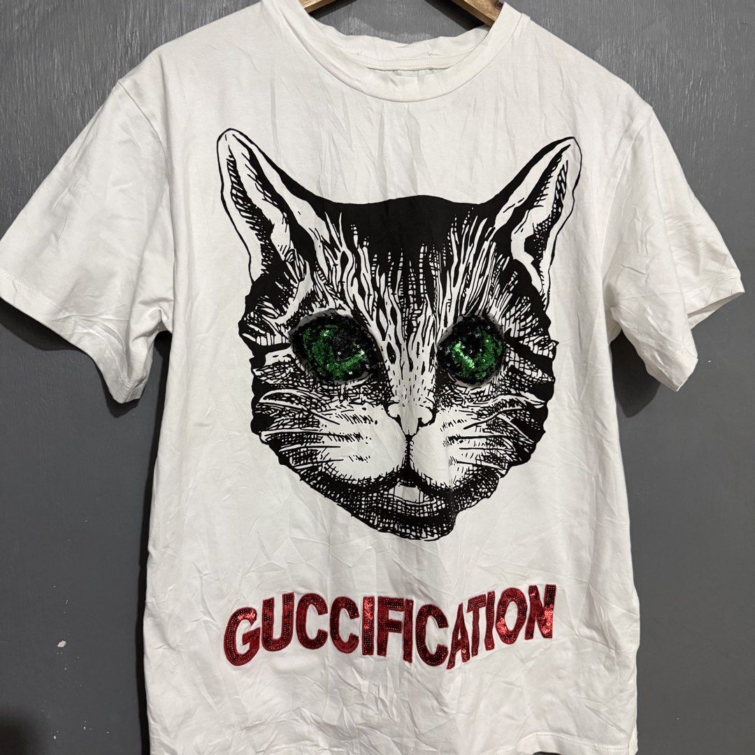 Gucci Cat Sequin T-Shirt (Category: Tshirts & Polo Shirts ) located in Manila. Submitted by preciousma24494 (Listing ID 1459814836, Image 2). Description: - Gucci T-shirt - Size: L - Design: Black cat graphic with green sequin eyes - Detail: 'GUCCIFICATION' text in red sequins - Origin: Made in Italy.