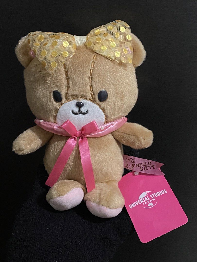 Hello Kitty Universal Studios Japan Teddy Bear Plush (Category: Plushies & Soft Toys) located in Davao. Submitted by hoowans_surplus (Listing ID 1459886900, Image 1). Description: - Super cute teddy bear plush from Universal Studios Japan. - Features a sparkly gold bow. - Adorned with a pink ribbon around its neck. - Original Kitty tag still attached. - Ideal for collectors or as a thoughtful gift. - Exceptionally soft and cuddly material..