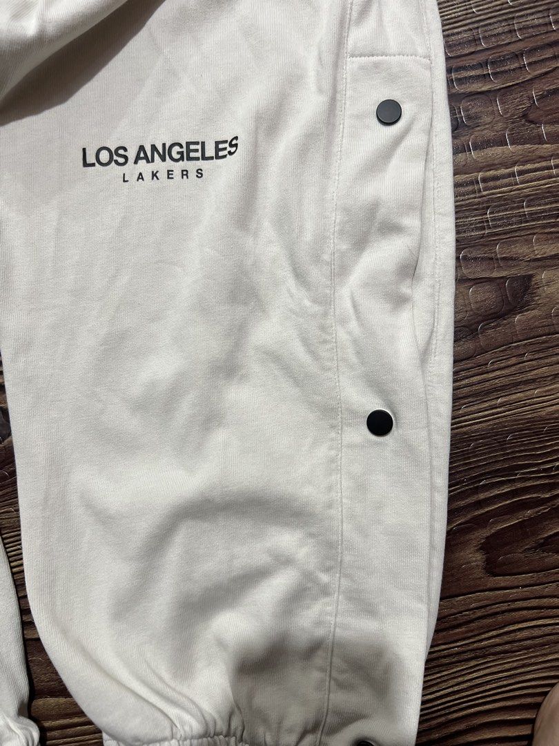 Los Angeles Lakers Snap Button Track Pants (Category: Joggers) located in Manila. Submitted by okeanos (Listing ID 1459759842, Image 3). Description: - Cream colored track pants - Los Angeles Lakers branding - Snap buttons down the sides for adjustable fit and style - NBA logo and embroidered logo on the front - Elastic waistband with drawstring - Cuffed ankles - Great for casual wear or game day.