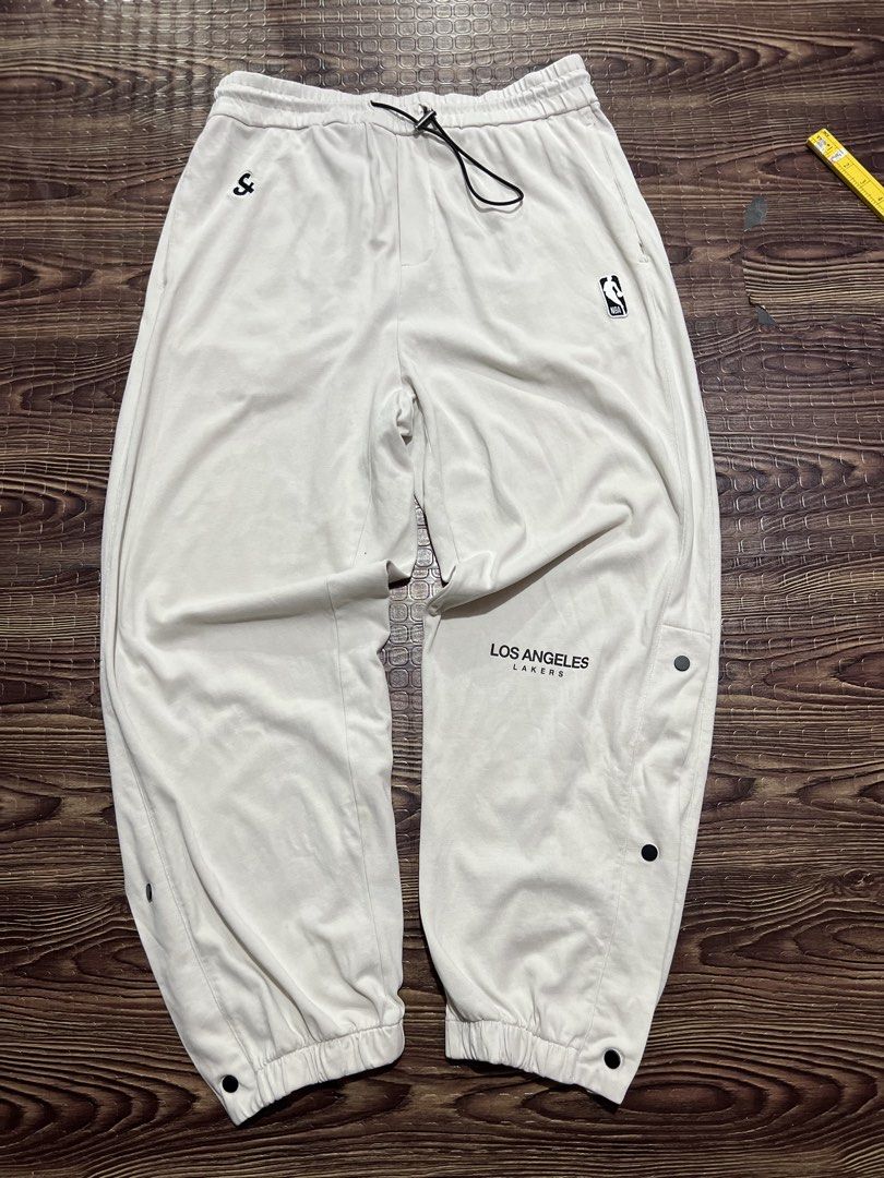 Los Angeles Lakers Snap Button Track Pants (Category: Joggers) located in Manila. Submitted by okeanos (Listing ID 1459759842, Image 1). Description: - Cream colored track pants - Los Angeles Lakers branding - Snap buttons down the sides for adjustable fit and style - NBA logo and embroidered logo on the front - Elastic waistband with drawstring - Cuffed ankles - Great for casual wear or game day.