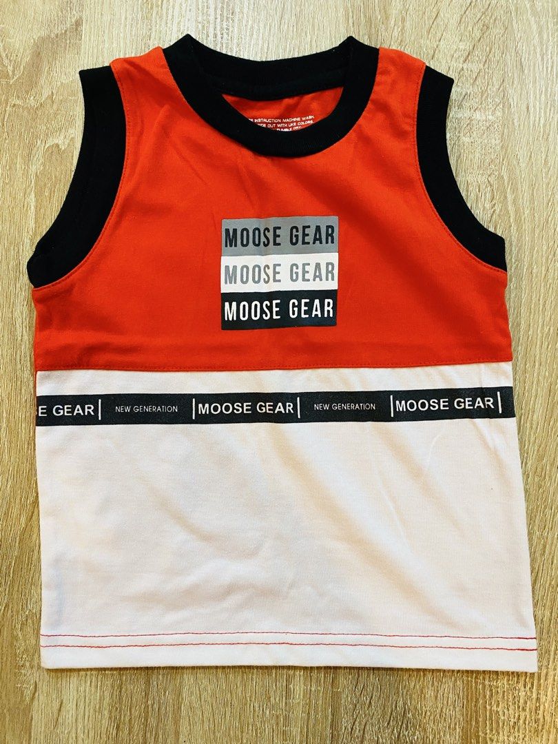 Moose Gear Orange & White Sleeveless Tank Top (Category: Babies & Kids Fashion) located in Indang. Submitted by matilde.sshop (Listing ID 1459888321, Image 1). Description: - Orange and white sleeveless tank top from Moose Gear. - Features multiple 'Moose Gear' prints on the front. - Black band around the waist with 'Moose Gear' and 'New Generation' text. - Black trim on neckline and armholes. - Red stitching at the hem. - Ideal for casual everyd