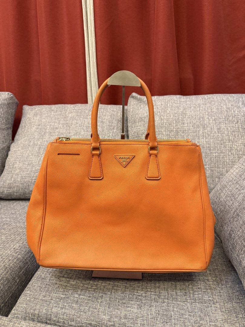 Prada Saffiano Lux Tote Orange (Category: Luxury Bags & Wallets) located in San Jose. Submitted by affordabletrendsby_cai (Listing ID 1459731119, Image 1). Description: - Authentic Orange Prada Saffiano Lux Tote - Elegant Gold Hardware - Secure Zipper Closure - Comfortable Top Handles - Signature Prada Triangle Logo - Spacious Interior for Essentials - Ideal for Everyday Errands or Travel.