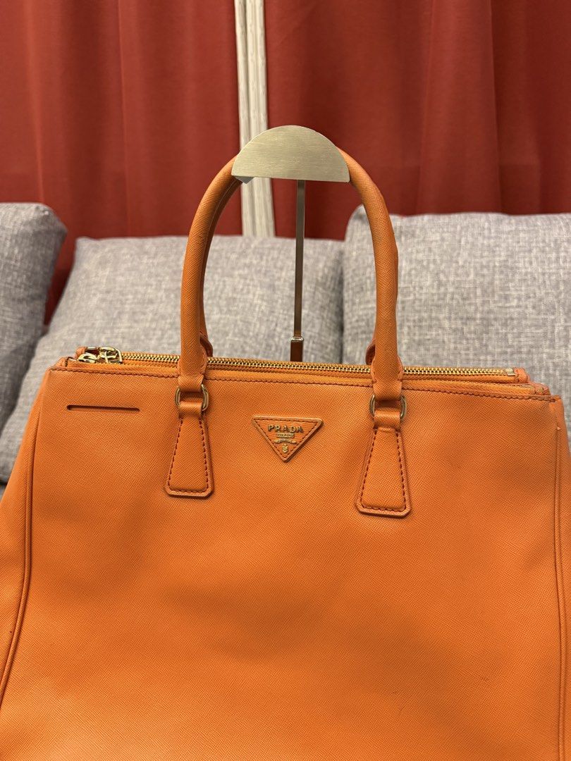Prada Saffiano Lux Tote Orange (Category: Luxury Bags & Wallets) located in San Jose. Submitted by affordabletrendsby_cai (Listing ID 1459731119, Image 2). Description: - Authentic Orange Prada Saffiano Lux Tote - Elegant Gold Hardware - Secure Zipper Closure - Comfortable Top Handles - Signature Prada Triangle Logo - Spacious Interior for Essentials - Ideal for Everyday Errands or Travel.