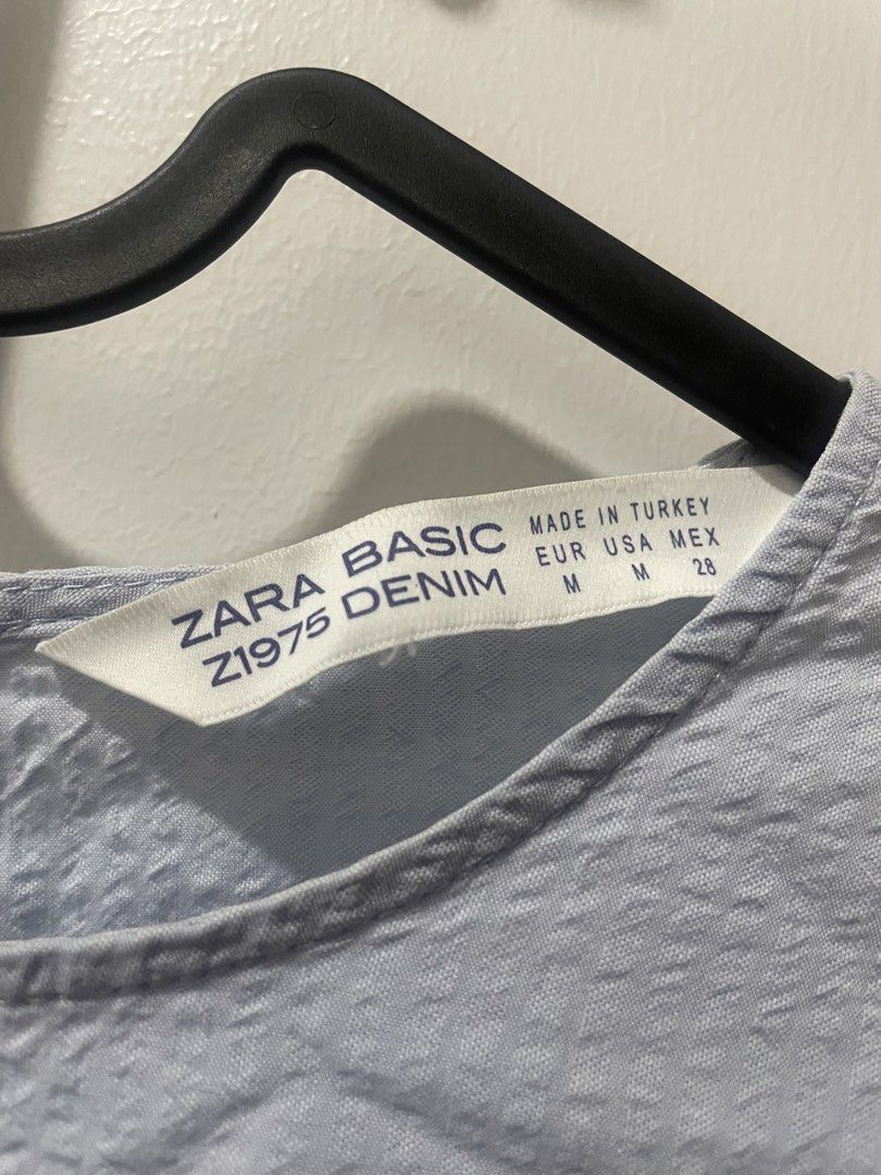 Zara Basic Denim Light Blue Puff Sleeve Top (Category: Blouses) located in Binan City. Submitted by dearlouise (Listing ID 1459847955, Image 2). Description: - Zara Basic light blue top - Features puff sleeves - Buttoned cuffs with pearl-like buttons - Textured fabric - Keyhole opening at the back with button closure - Flaw: missing pearl button (right cuff).