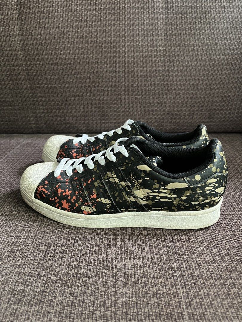 Adidas Superstar Camo Splatter Sneakers (Category: Sneakers) located in Manila. Submitted by lowkeyxan (Listing ID 1459985728, Image 1). Description: Original, Adidas Superstar sneakers with a black base, featuring a cool camo splatter design in orange and gold. Classic shell toe and white laces. Perfect for everyday style. .